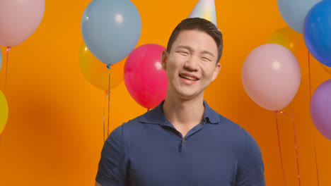 Studio-Portrait-Of-Man-Wearing-Party-Hat-Celebrating-Birthday-With-Balloons-And-Party-Blower-2